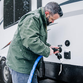 Camco rolled hose next to tape measure showing 25-foot scale for storage and transport convenience