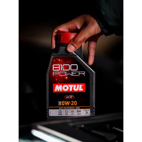 Motul 8100 Power bottle beside an engine bay for maintenance convenience
