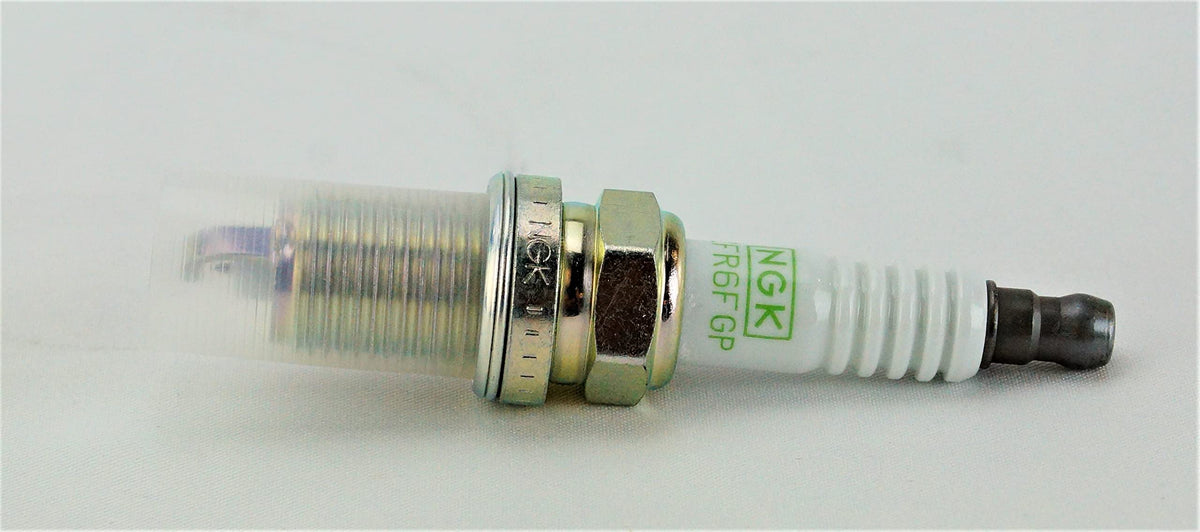Pack of four NGK spark plugs arranged on white surface demonstrating complete replacement set