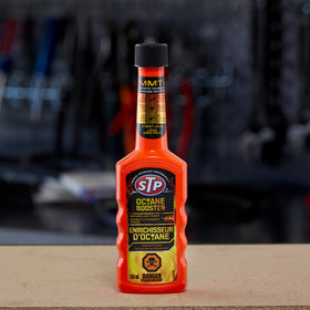 STP Octane Booster bottle next to a fuel pump showing bottle size and treatment benefit