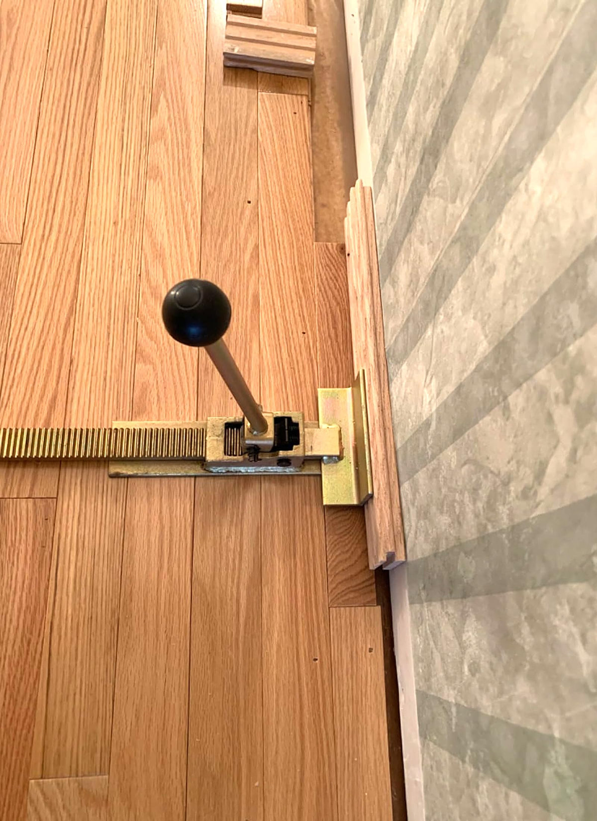 Swellisher flooring jack in use on last row showing tight fit near wall for precise alignment