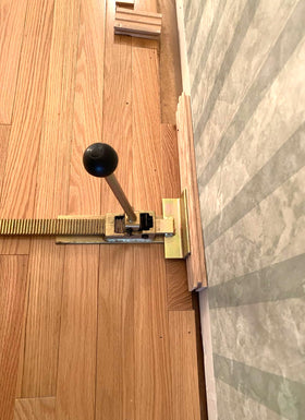 Swellisher flooring jack in use on last row showing tight fit near wall for precise alignment
